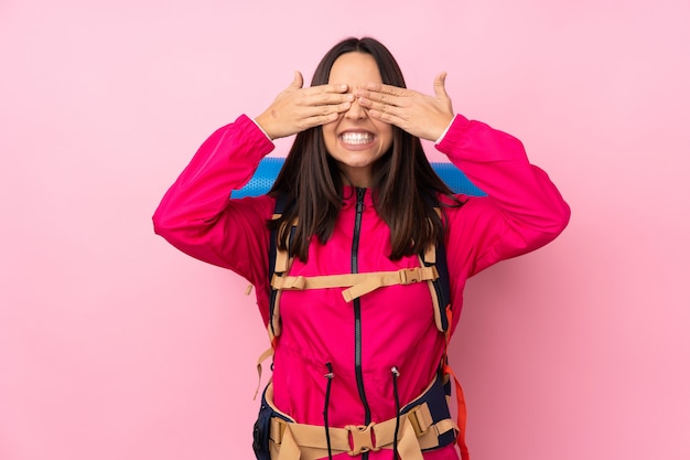 Mulher jovem alpinista com uma mochila grande sobre parede rosa isolada, cobrindo os olhos pelas mãos