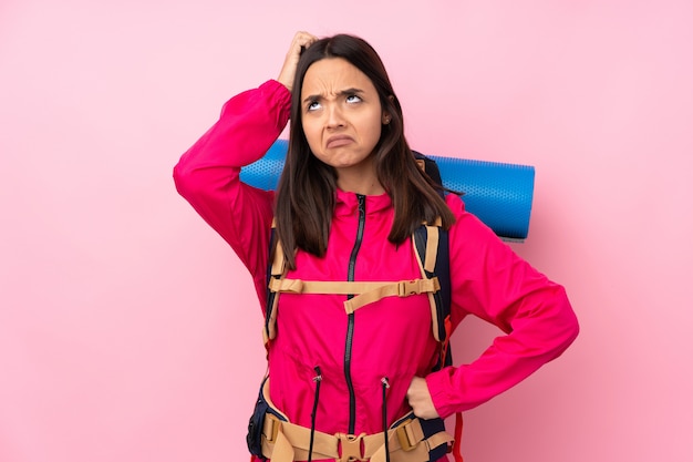 Mulher jovem alpinista com uma mochila grande, tendo dúvidas enquanto coça a cabeça