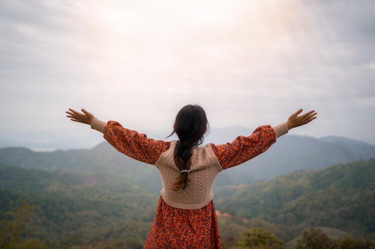 Foto mulher jovem animada de pé no pico da montanha braços estendidos liberdade e felicidade realização nas montanhas visão de trás