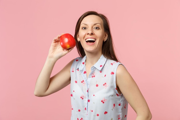 Mulher jovem animada em roupas de verão segurando frutas frescas de maçã vermelha madura isoladas no fundo da parede rosa pastel, retrato de estúdio. Estilo de vida vívido de pessoas, relaxe o conceito de férias. Mock up espaço de cópia.
