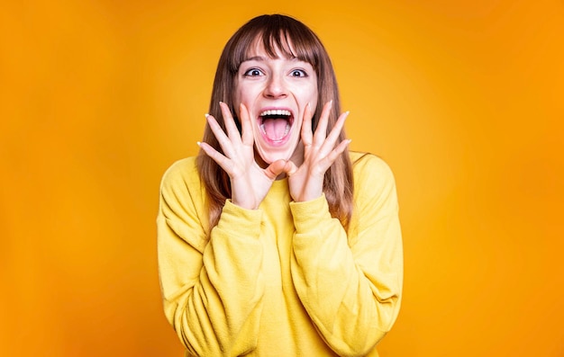 Mulher jovem animada gritando em um retrato de estúdio de fundo amarelo - Garota feliz anunciando notícias em voz alta - Mulher adorável adorável feliz regozija-se com sucesso - Conceito de expressão facial