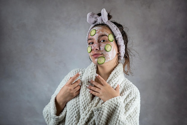 Mulher jovem aplicando máscara de limpeza facial com creme e fatias de pepino Saúde de sua pele
