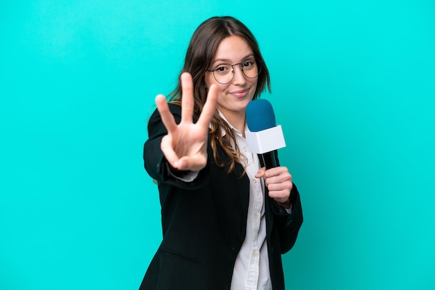 Mulher jovem apresentadora de TV isolada em fundo azul feliz e contando três com os dedos