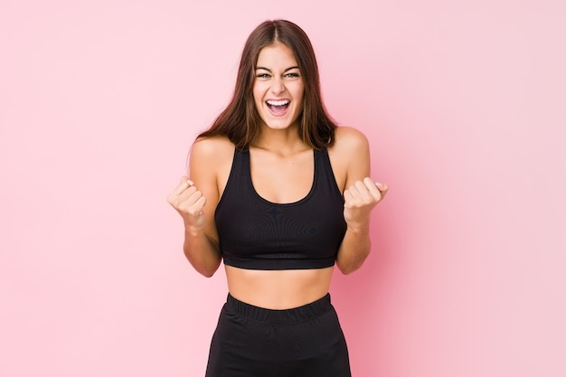 Mulher jovem aptidão caucasiana fazendo esporte isolado torcendo despreocupado e animado. Conceito de vitória.