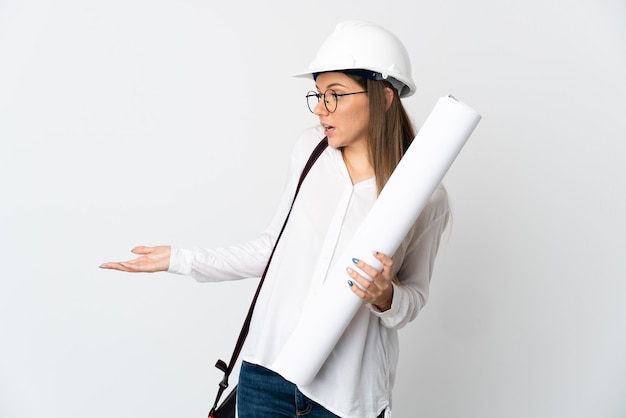 Foto mulher jovem arquiteta lituana com capacete e segurando plantas isoladas na parede branca com expressão de surpresa enquanto olha para o lado