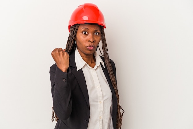 Mulher jovem arquiteto americano africano isolada no fundo branco, mostrando o punho para a câmera, expressão facial agressiva.