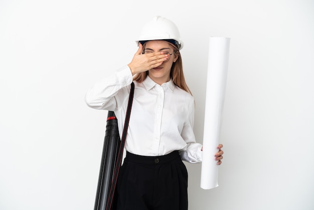 Mulher jovem arquiteto com capacete e segurando plantas isoladas na parede branca, cobrindo os olhos pelas mãos. não quero ver nada