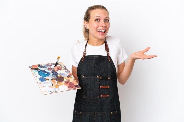 Mulher jovem artista caucasiana segurando uma paleta isolada no fundo branco com expressão facial chocada