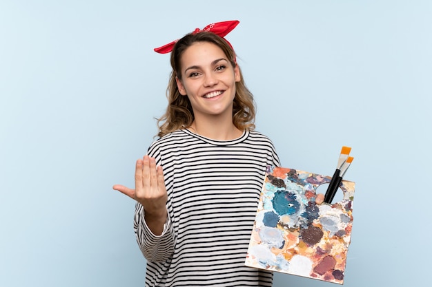 Mulher jovem artista segurando uma paleta azul convidando para vir com a mão