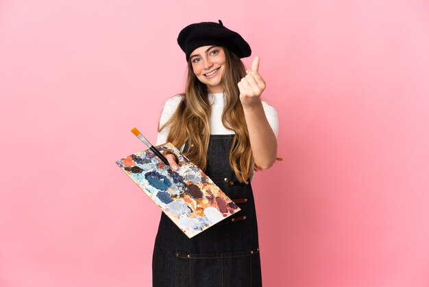 Mulher jovem artista segurando uma paleta isolada em rosa fazendo gesto de dinheiro