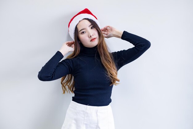 Mulher jovem asiática bonita do retrato no traje do Natal e usar chapéu de Papai Noel vermelho com sorriso no fundo branco e espaço de cópia. Feliz por uma mulher adolescente no tema Natal.