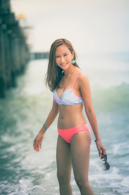 Mulher jovem asiática bonita usando biquíni na praia com uma cara sorridente