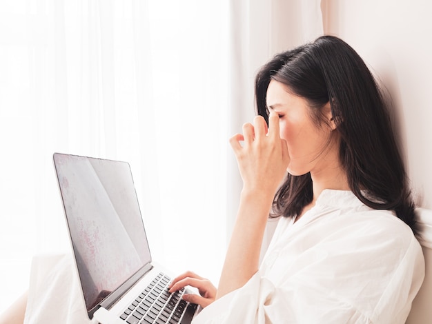 Mulher jovem asiática esfregando os olhos cansados ao usar o laptop.