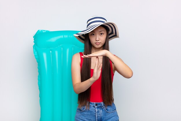 Mulher jovem asiática olhando séria, severa, zangada e descontente, fazendo sinal de tempo limite. conceito de verão