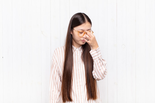 Mulher jovem asiática se sentindo estressada, infeliz e frustrada, tocando a testa e sofrendo de enxaqueca ou forte dor de cabeça