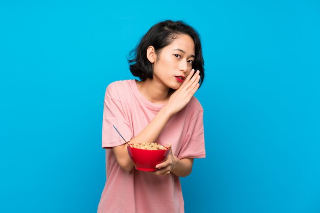 Mulher jovem asiática segurando uma tigela de cereais sussurrando algo
