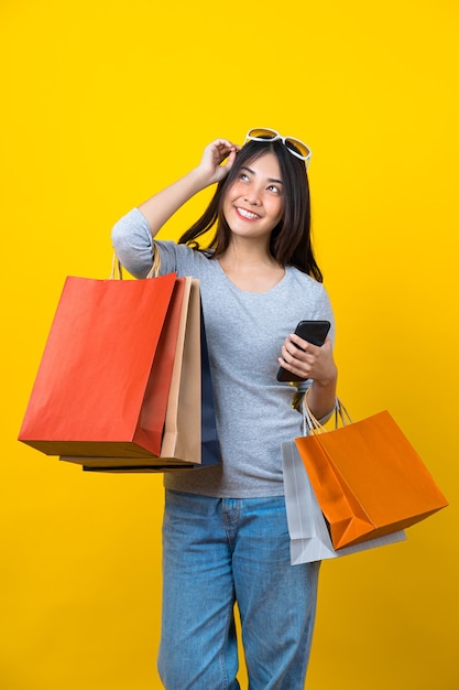 Mulher jovem asiática sorridente e atraente carregando um celular com uma sacola coloful de compras