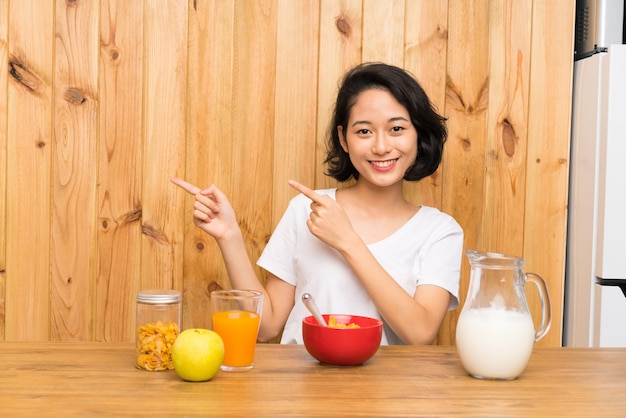 Mulher jovem asiática tomando café da manhã leite apontando o dedo para o lado