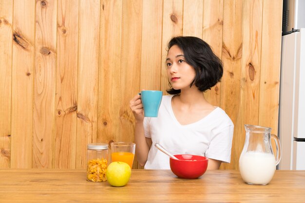 Mulher jovem asiática tomando café da manhã segurando uma xícara de café