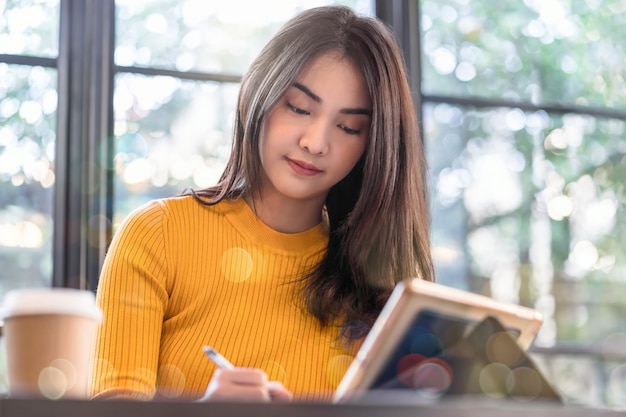 Mulher jovem asiática trabalhando e usando laptop de tecnologia em uma cafeteria moderna ou espaço de coworking