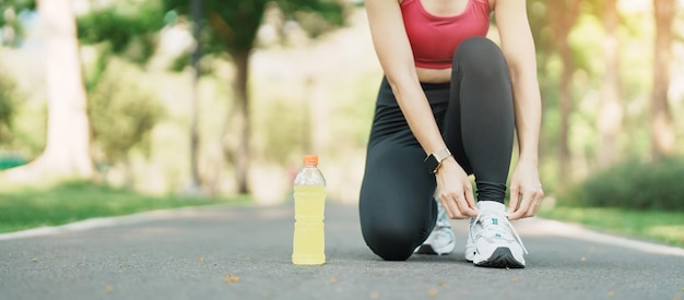 Mulher jovem atleta amarrando tênis de corrida com corredor feminino Energy Drink water pronto para fazer jogging fora da Ásia Fitness andando e exercitando no parque manhã bem-estar bem-estar e conceitos esportivos