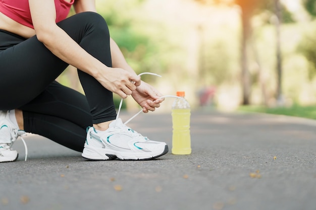 Mulher jovem atleta amarrando tênis de corrida com corredor feminino Energy Drink water pronto para fazer jogging fora da Ásia Fitness andando e exercitando no parque manhã bem-estar bem-estar e conceitos esportivos