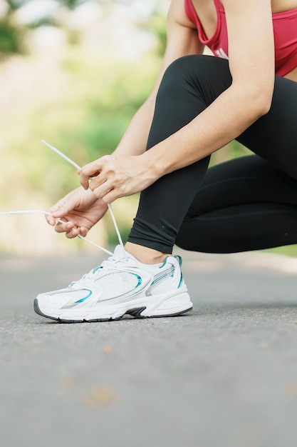 Mulher jovem atleta amarrando tênis no corredor feminino ao ar livre do parque pronto para fazer jogging na estrada fora da Ásia Fitness andando e exercitando na trilha em conceitos de bem-estar e esporte matinais