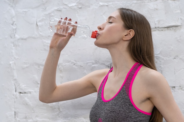 Mulher jovem atleta faz uma pausa para beber água de uma garrafa de plástico.