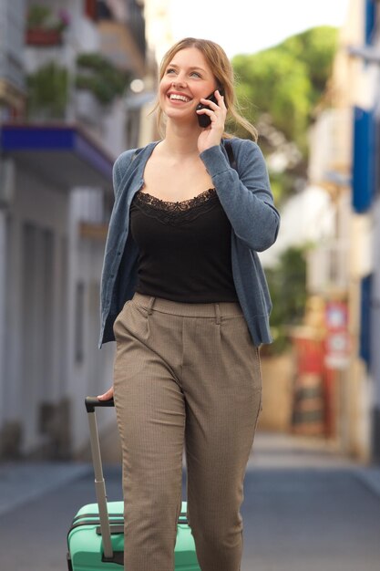 Mulher jovem atraente a caminhar com uma mala e a falar ao telemóvel.