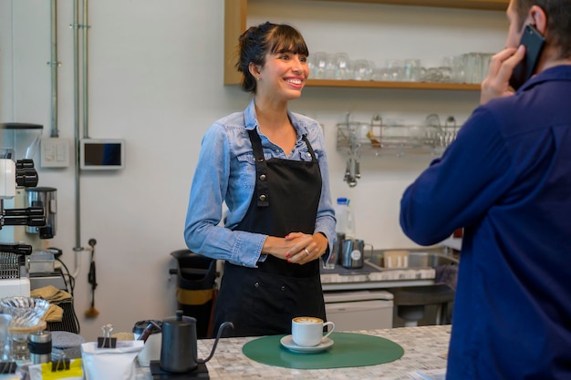 Mulher jovem barista de serviço com cliente na cafeteria
