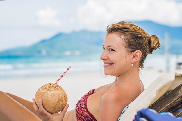 Mulher jovem bebendo leite de coco em uma espreguiçadeira na praia