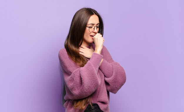 Mulher jovem, bem casual, sentindo-se mal, com dor de garganta e sintomas de gripe, tosse com a boca coberta