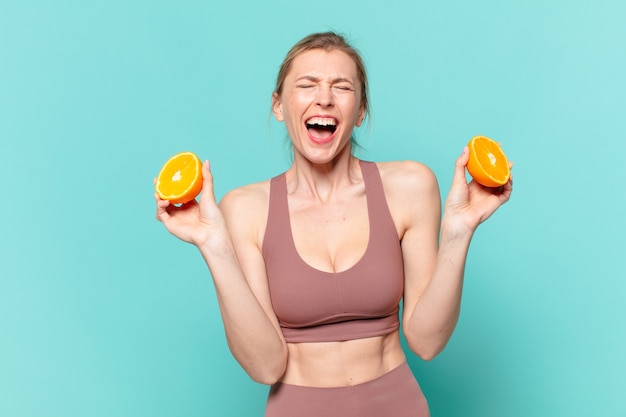 Mulher jovem bonita com expressão de raiva e segurando uma laranja