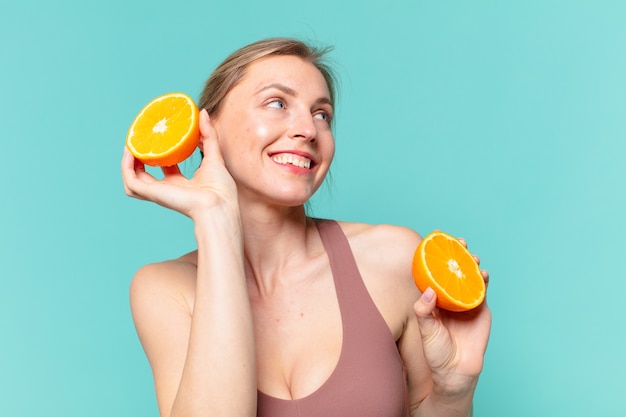 Mulher jovem bonita com expressão feliz e segurando uma laranja