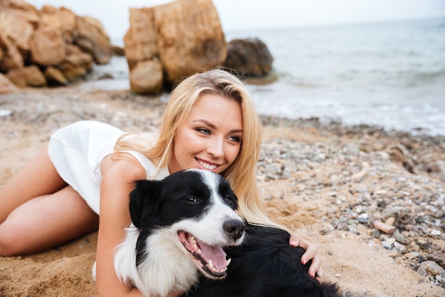 Mulher jovem bonita e alegre abraçando o cachorro na praia