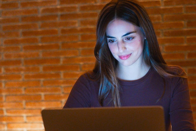 Foto mulher jovem, bonita e sorridente usando laptop em casa à noite, garota feliz olhando para o computador, pessoas alegres sentadas na mesa na sala de estar, conceito de teletrabalho empreendedor e pessoa trabalhadora.