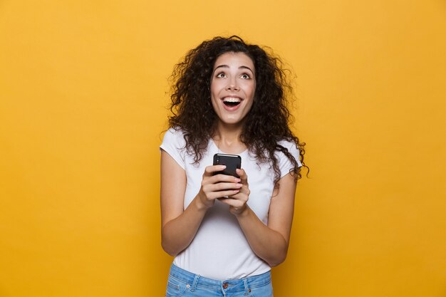 Mulher jovem bonita feliz posando isolada em amarelo usando telefone celular.