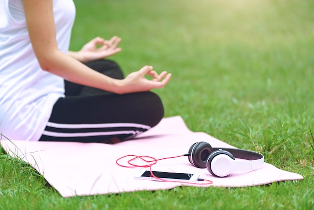 Mulher jovem bonita ioga na grama de verão com fones de ouvido, ouvir música e relaxar