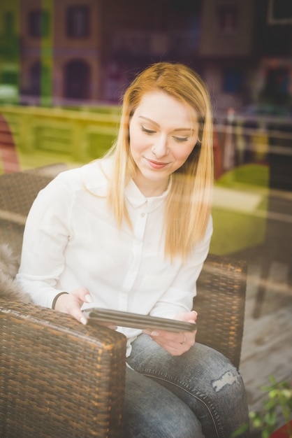 mulher jovem bonita loira de cabelo liso na cidade sentado no restaurante usando tablet