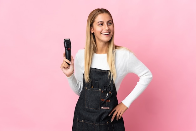 Mulher jovem cabeleireira isolada na parede rosa posando com os braços na cintura e sorrindo