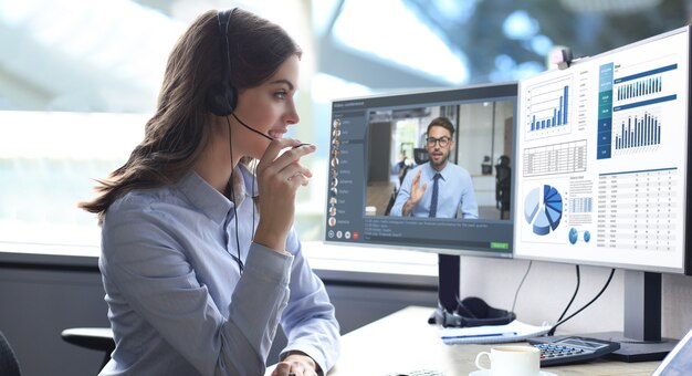 Mulher jovem call center trabalhando no computador, fazendo videoconferência com colegas no PC. Discutindo o relatório financeiro de sua empresa. Trabalho à distância. Coronavírus.