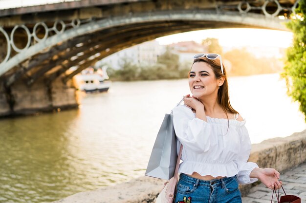 Mulher jovem caminhando à beira do rio com o pôr do sol ao fundo, depois de ir às compras