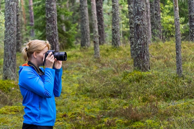 Mulher jovem, caminhando entre árvores e tirando fotos com a câmera. fotógrafo de mulher de meia-idade tirando foto na floresta de outono. fotografia da natureza.