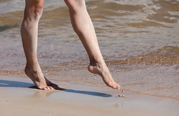 Mulher jovem caminhando na praia. Pernas femininas na areia à beira-mar