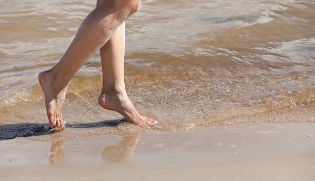 Mulher jovem caminhando na praia. Pernas femininas na areia à beira-mar