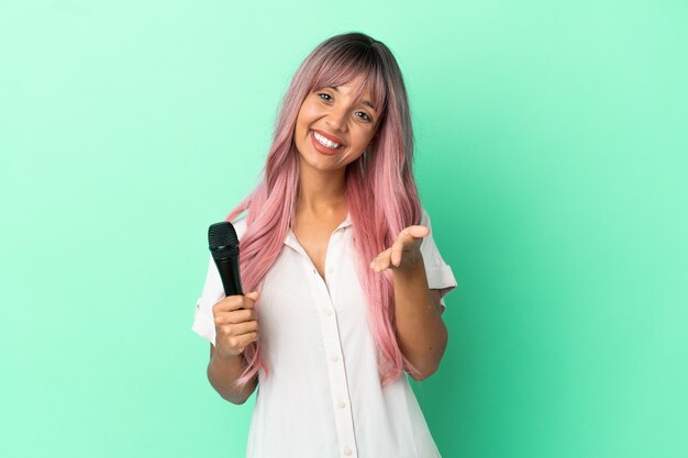 Mulher jovem cantora de raça mista com cabelo rosa isolado em um fundo verde apertando as mãos para fechar um bom negócio