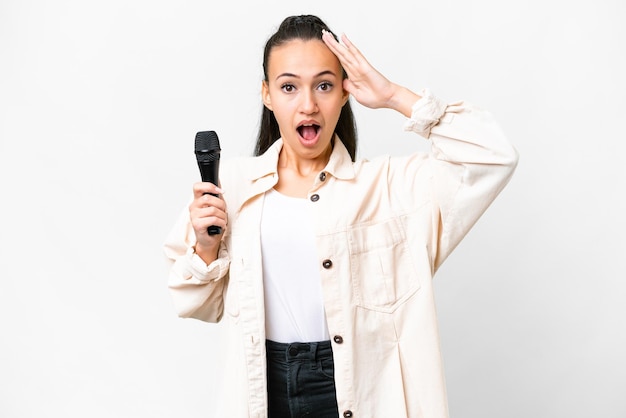 Mulher jovem cantora pegando um microfone sobre fundo branco isolado com expressão de surpresa