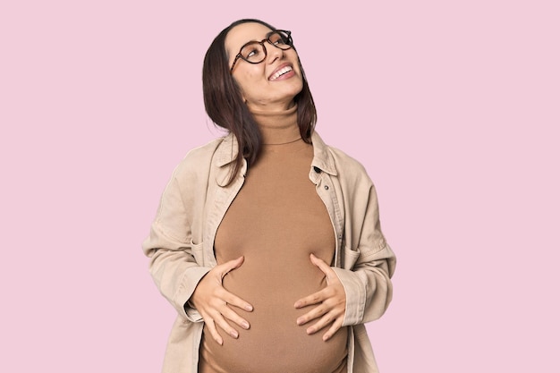 Mulher jovem caucasiana grávida mostrando a maternidade no fundo do estúdio relaxada e feliz rindo