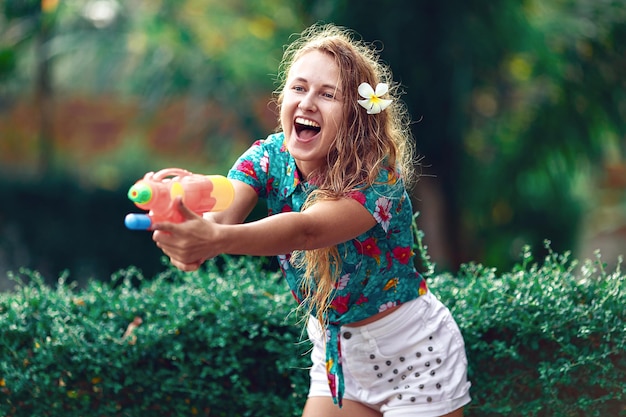 Mulher jovem caucasiana luta com pistola de água no festival Songkran. Conceito de férias / ano novo tailandês