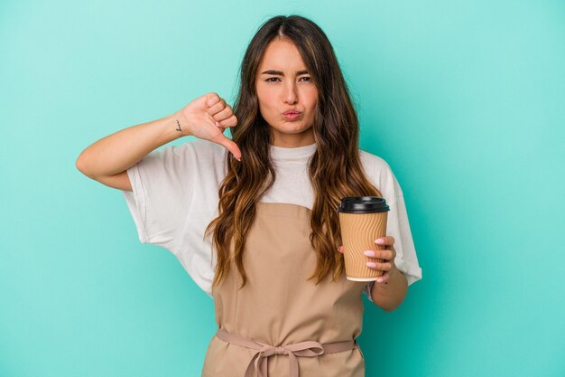 Mulher jovem, caucasiano, balconista segurando um café para viagem isolado em um fundo azul, sente-se orgulhosa e autoconfiante, exemplo a seguir.